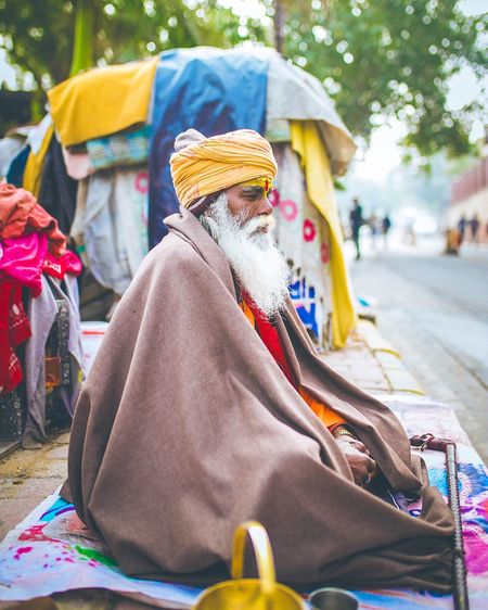 Side view of sadhu sitting on sidewalk in city