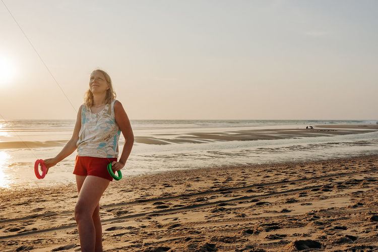 Woman looking up while standing at beach during sunset
