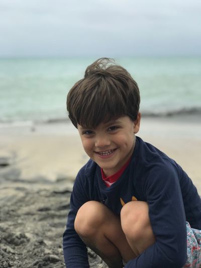 Portrait of smiling boy crouching on sand at beach