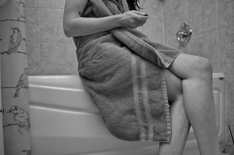 Midsection of woman wrapped in towel sitting on bathtub at home