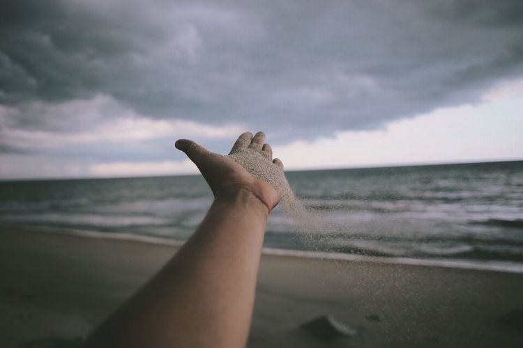 Cropped hand with sand at beach against sky