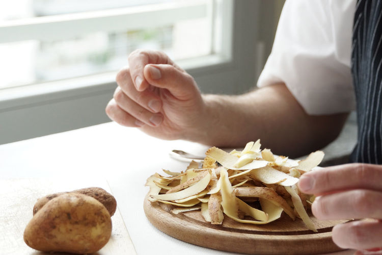 Cropped image of chef peeling potatoes on table