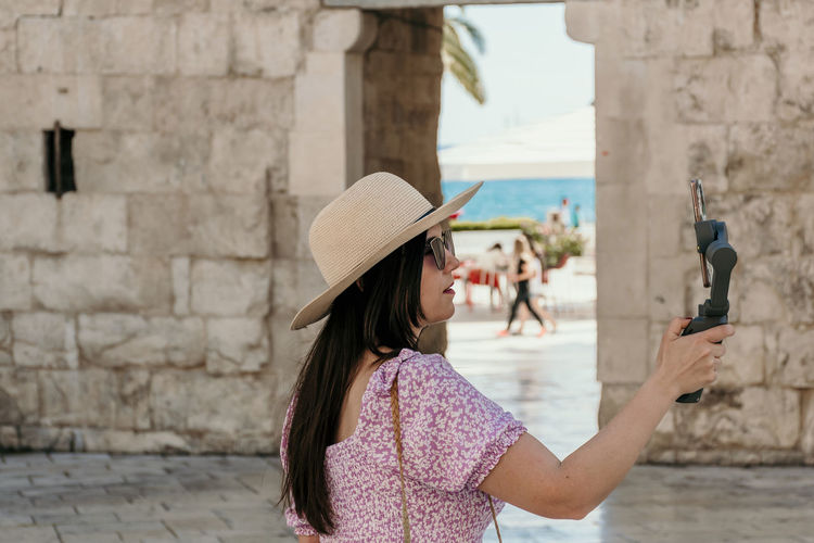 Side view of young woman using gimbal and mobile phone for vlogging on her travels.