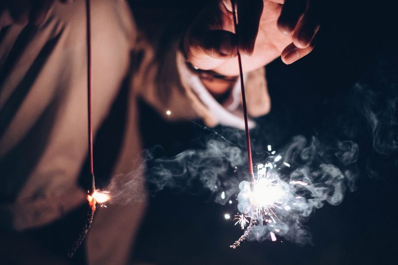 Midsection of woman holding lit sparklers at night