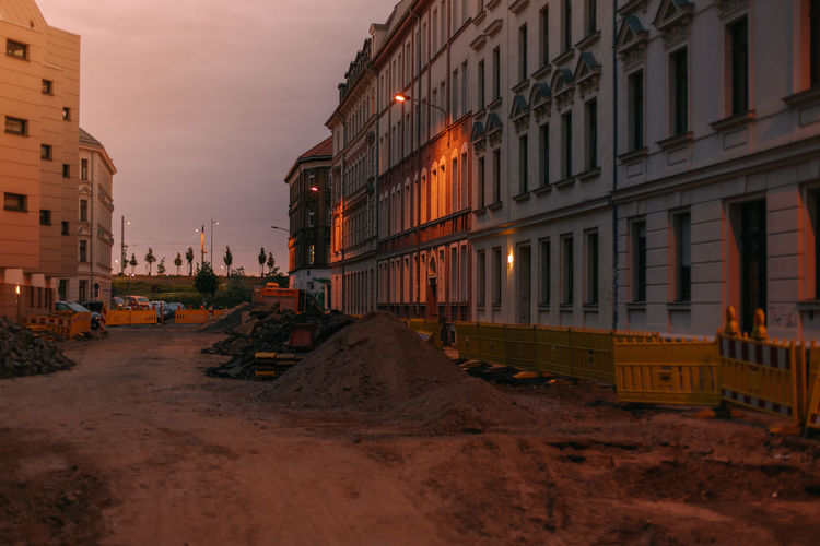 Road by buildings against sky during sunset