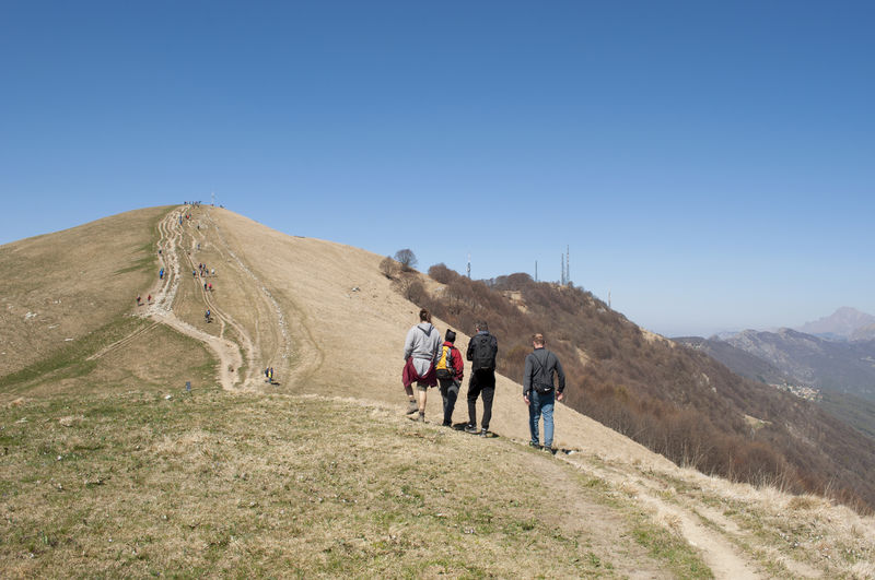 Rear view of people walking on mountain against clear blue sky