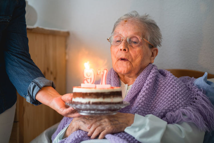 Old woman blows the candles from his 96th birthday cake with daughter