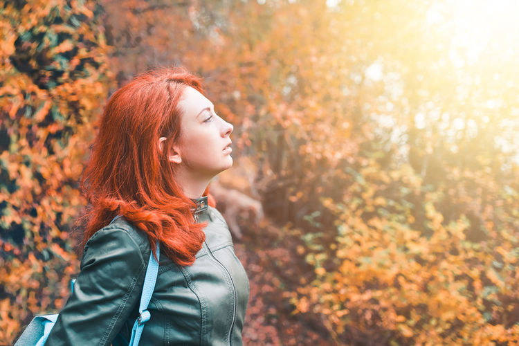 Young woman looking away in forest during autumn