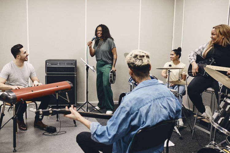 Happy multiracial men and women looking at friend singing during rehearsal in classroom