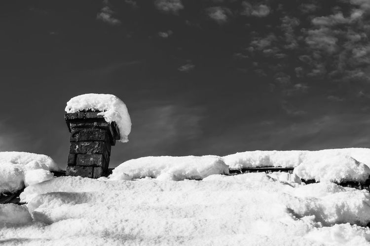 Roof of a house with chimney covered snow against a blue sky black and white photo