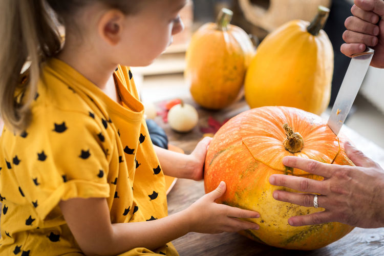 Cropped hand cutting pumpkin with girl sitting a home