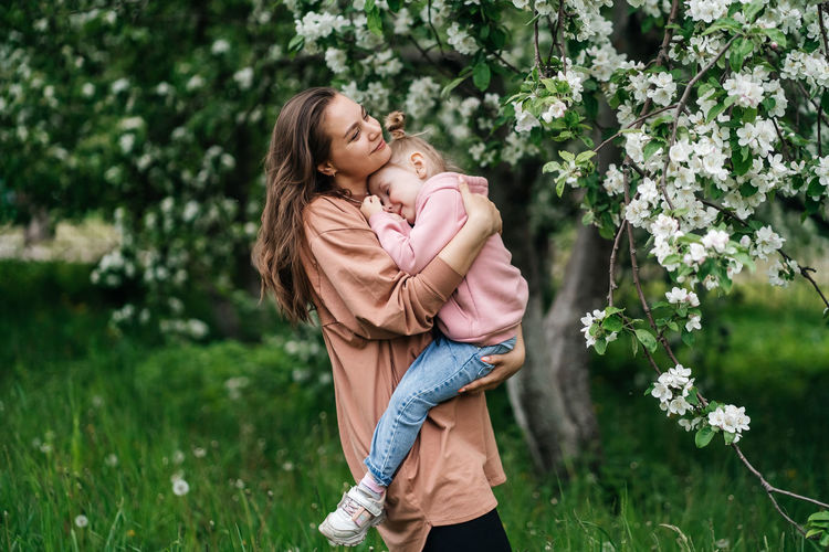 Young mother with her daughter in her arms in a blooming apple orchard