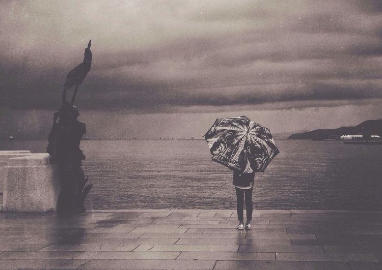 Woman standing by sea against cloudy sky
