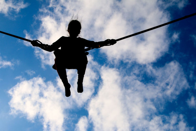 Low angle view of silhouette girl bungee jumping against sky