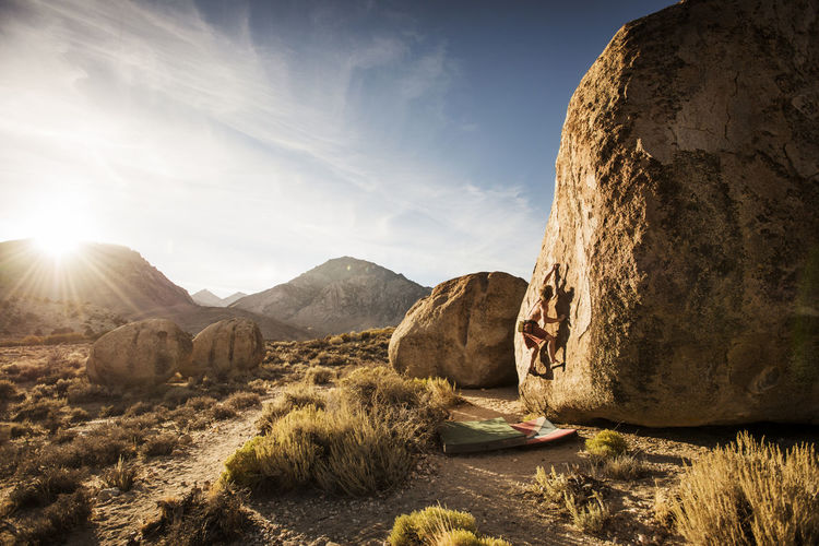 Shirtless man climbing rock against sky on sunny day