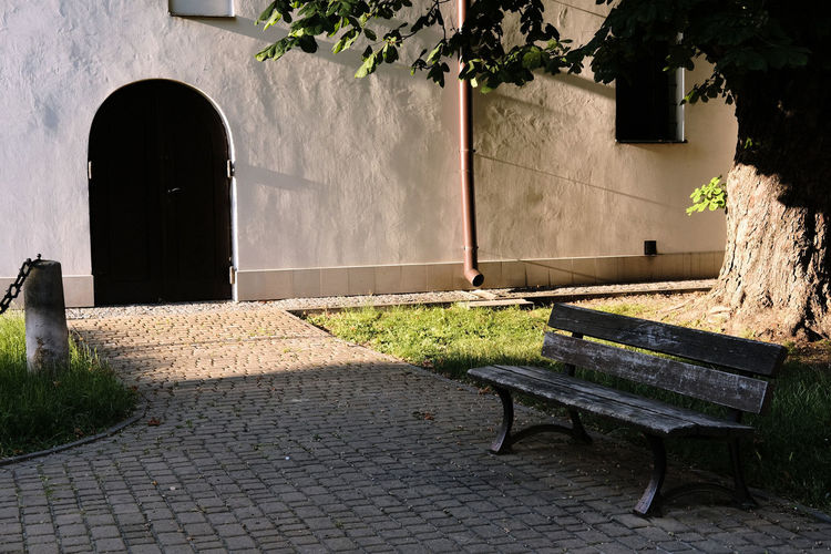 Bench on sidewalk by wall against building