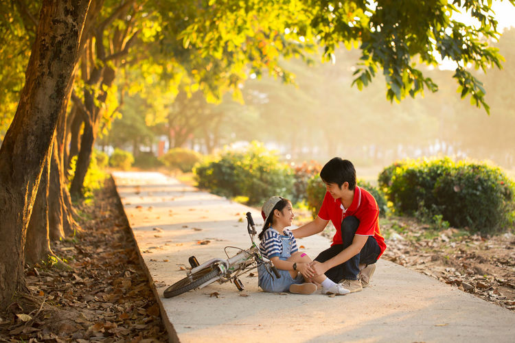 Father healing daughter while sitting on footpath at park