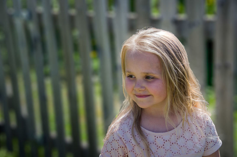 Smiling girl looking away against fence 