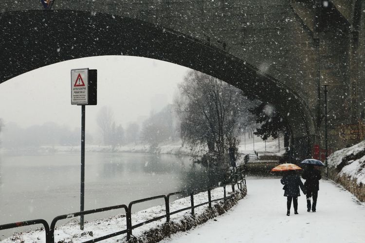 People walking on road by frozen river in city