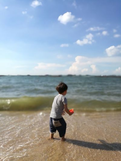 Rear view of boy in sea against sky on sunny day