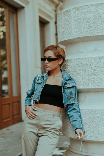 Young woman wearing sunglasses standing against built structure