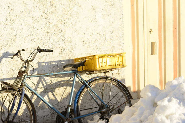 An antique bike with an empty yellow pot parked in front of cement wall beside doorway