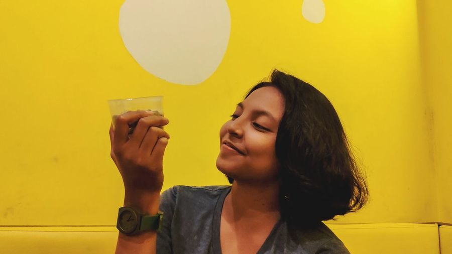 Portrait of smiling young woman standing against yellow wall at home