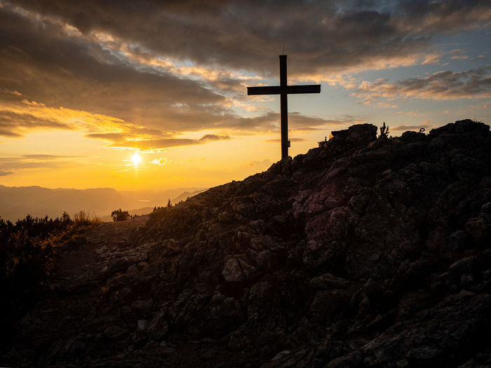 Silhouette cross on mountain against sky during sunset