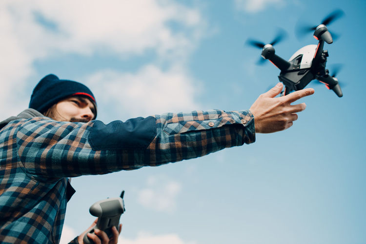 Low angle view of man holding drone against sky