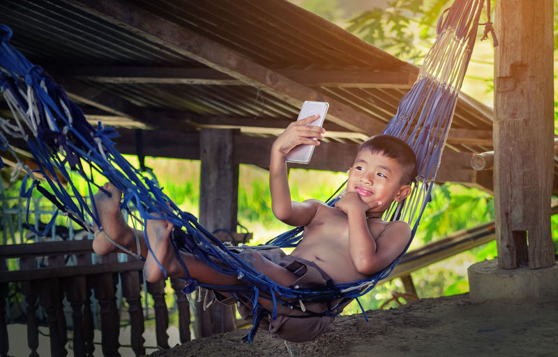 Cute boy lying on hammock taking selfie from smart phone