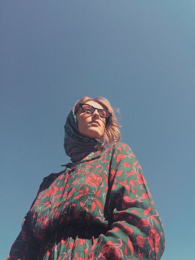 LOW ANGLE VIEW OF WOMAN LOOKING AT CAMERA AGAINST SKY