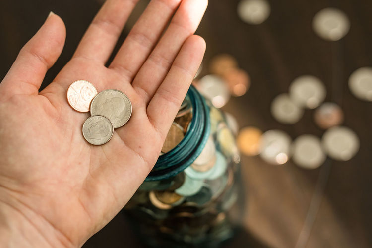 Woman putting coins into jar, saving money, penny pinching
