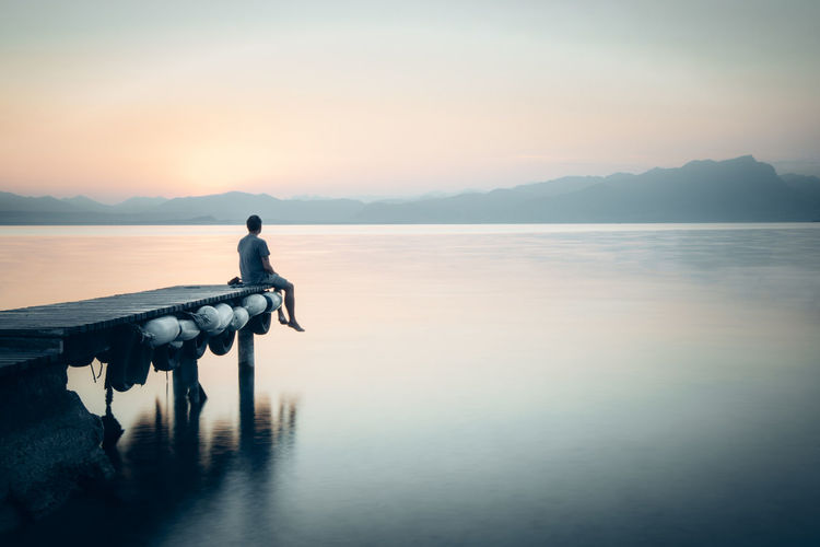 Italy, lazise, man sitting on jetty looking at lake garda
