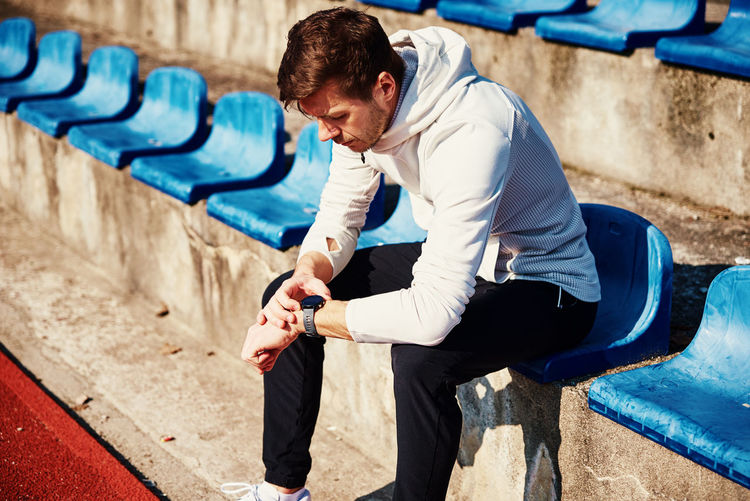 Man sitting at stadium seat and checking fitness watch after exercises