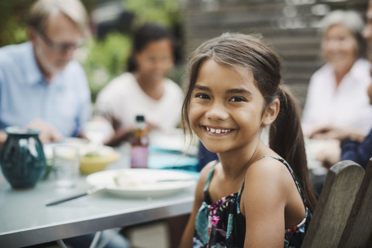 Portrait of happy girl sitting with family at dining table in yard
