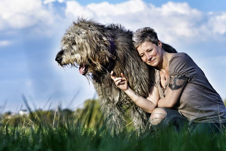 Happy woman with irish wolfhound on grassy field against sky