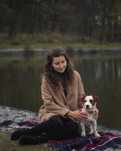 Full length of woman with dog sitting by lake