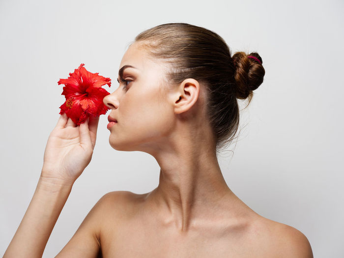 Portrait of woman holding red flower against white background