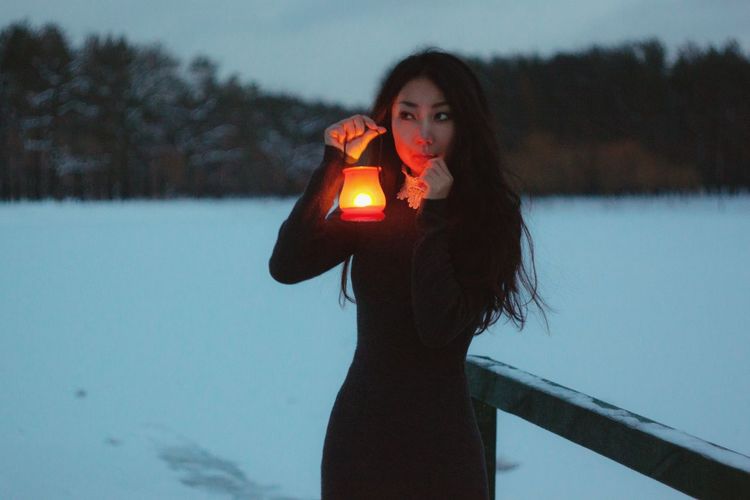 Woman holding illuminated lantern while standing in snow