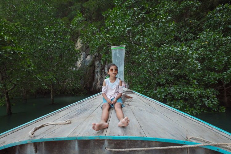 Full length of girl sitting on boat deck against trees