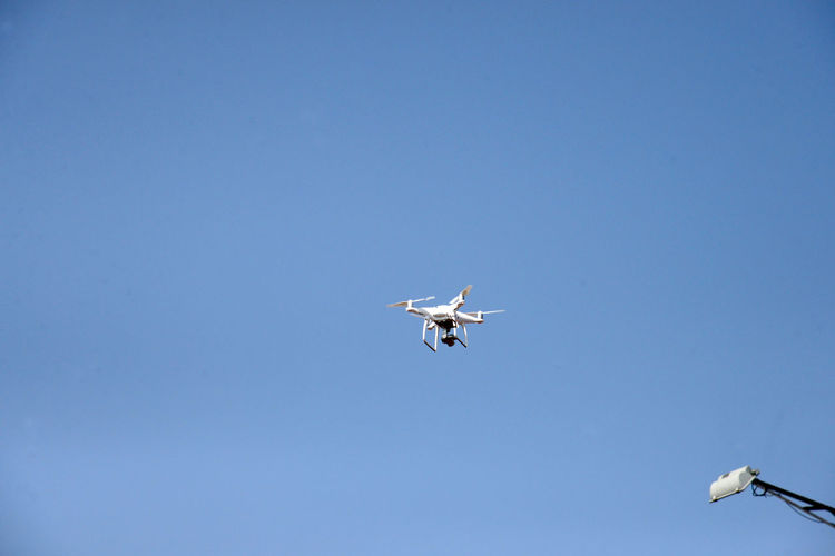 Low angle view of drone flying against clear blue sky
