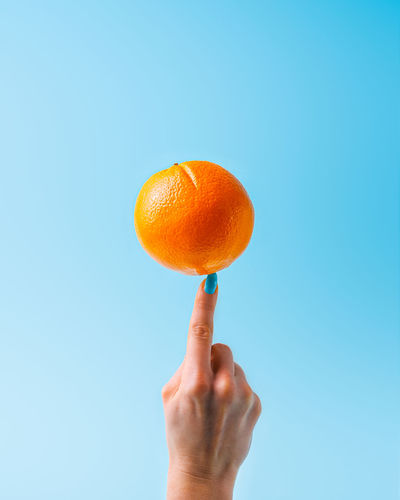 Woman balancing an orange on index finger on blue background