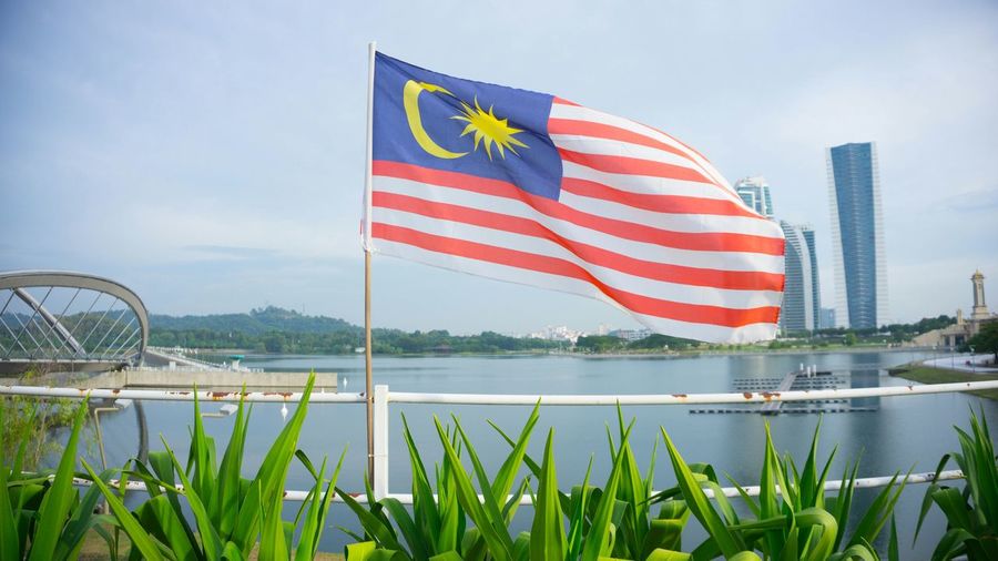 Malaysian flag waving against lake in city