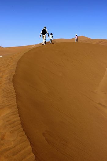 Man on sand dune in desert against clear sky