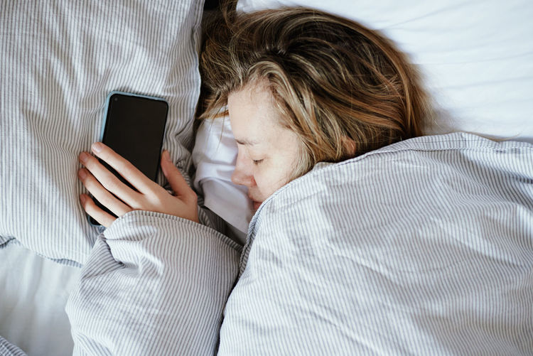 Caucasian woman sleeping in bed and hold smartphone in hand