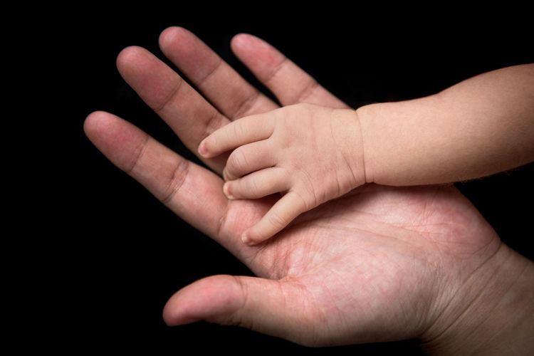 Close-up of person holding baby hand over black background