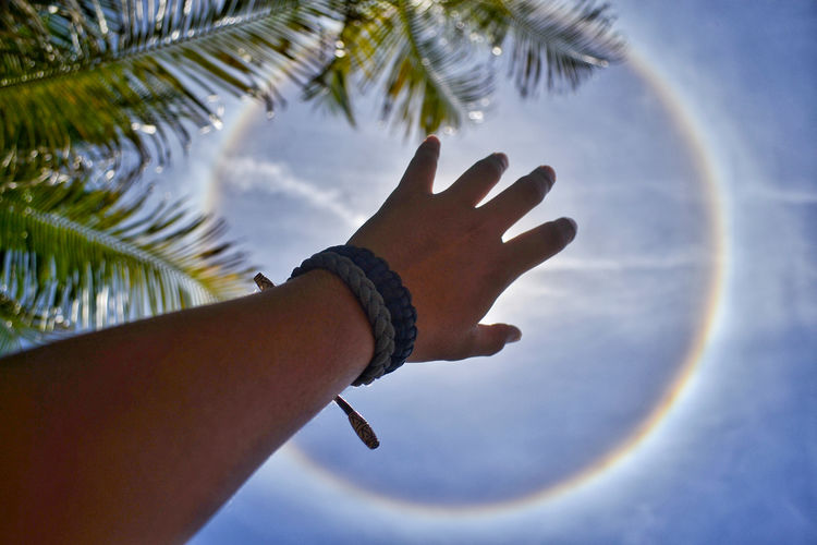 Low angle view of cropped hand hiding sun against sky