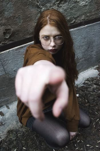 Portrait of young woman pointing while kneeling on sidewalk