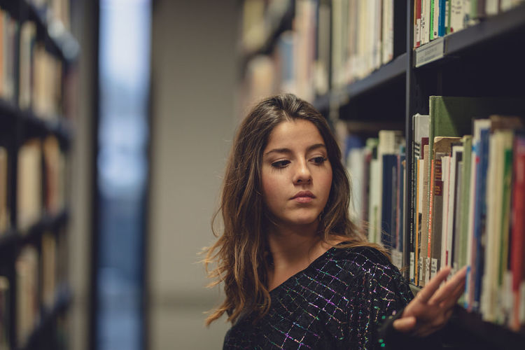 Young woman standing by bookshelf at library