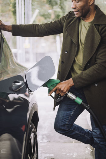 Mature man pumping gas in car while standing at fuel station